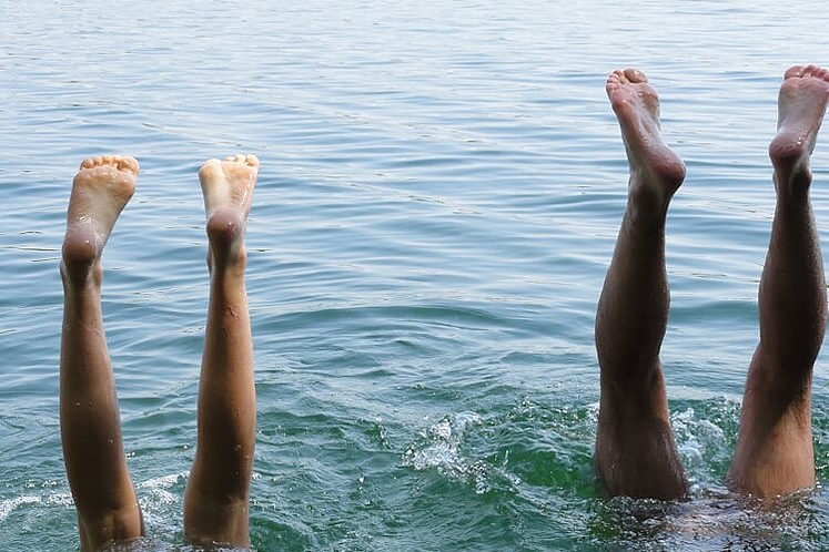 Ein Paar macht einen Kopfstand im Wasser und streckt die Füße in die Luft.