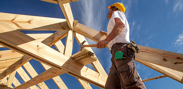 Ein Handwerker steht auf einer Holzkonstruktion von einem neuen Dach. 