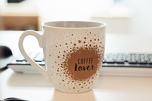 Kaffeetasse mit der Aufschrift 'Coffee Lover' steht auf einem Schreibtisch zwischen Computerbildschirmen.