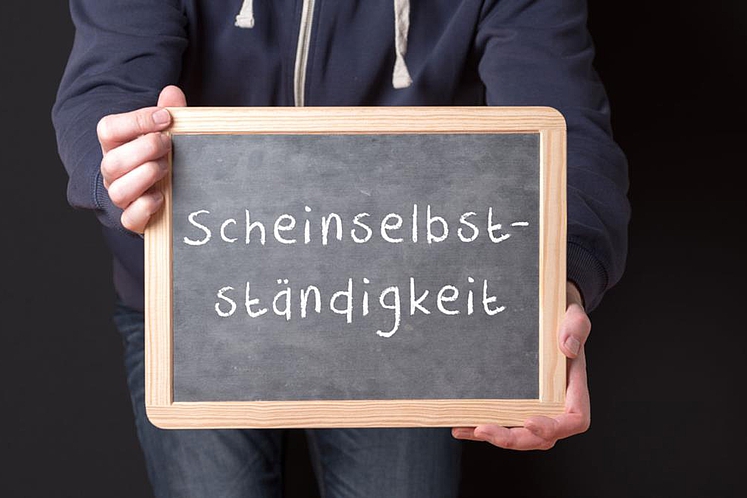 Arbeitnehmer hält Tafel mit Aufschrift „Scheinselbstständigkeit“