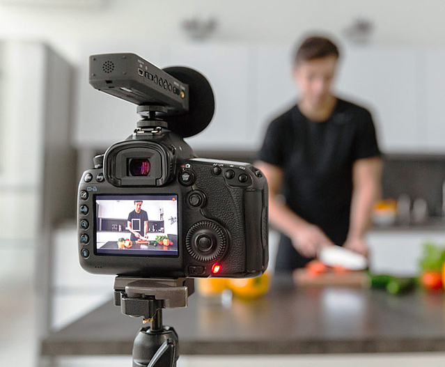 Filmdreh für ein gastronomisches Unternehmen. Kamera filmt Mann beim Schneiden von Gemüse.