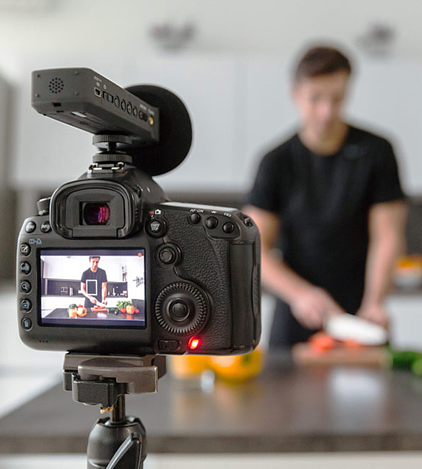 Filmdreh für ein gastronomisches Unternehmen. Kamera filmt Mann beim Schneiden von Gemüse.