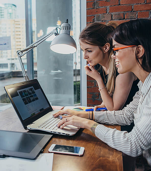 Zwei Frauen arbeiten am Design einer Website und nutzen einen Laptop um Bilder zu suchen.